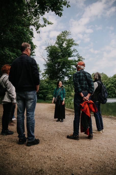 Gruppe von Personen steht auf einem Weg in der Natur, eine Person spricht zu ihnen.