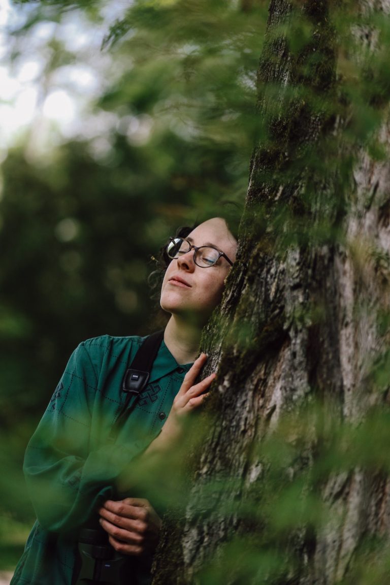 Eine Person mit Brille lehnt an einem Baum und genießt die Natur.